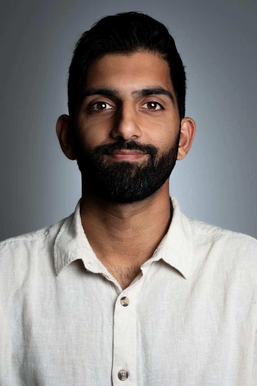 An editorial portrait of a CityRise team member against a graduated grey studio backdrop, cream linen shirt, lit from the left with a single soft key