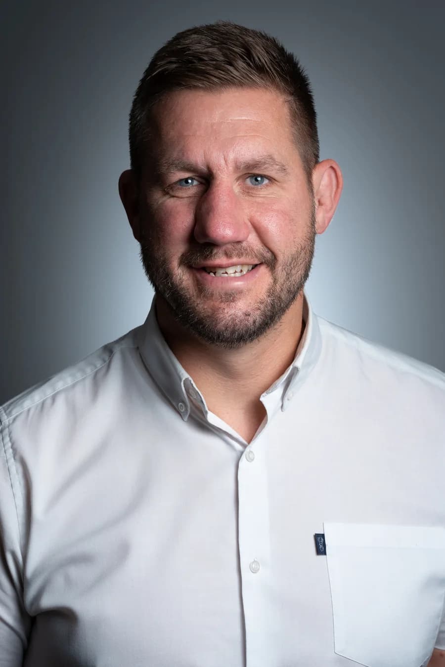 An editorial portrait of a CityRise team member against the same graduated grey backdrop, white shirt, the same key light and the same framing