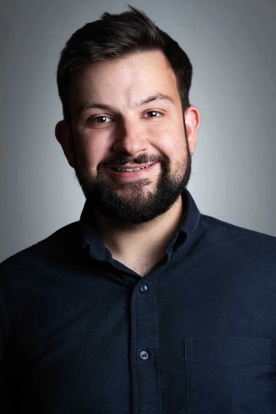 An editorial portrait of a CityRise team member against the same graduated grey backdrop, navy shirt, the same key light and the same framing