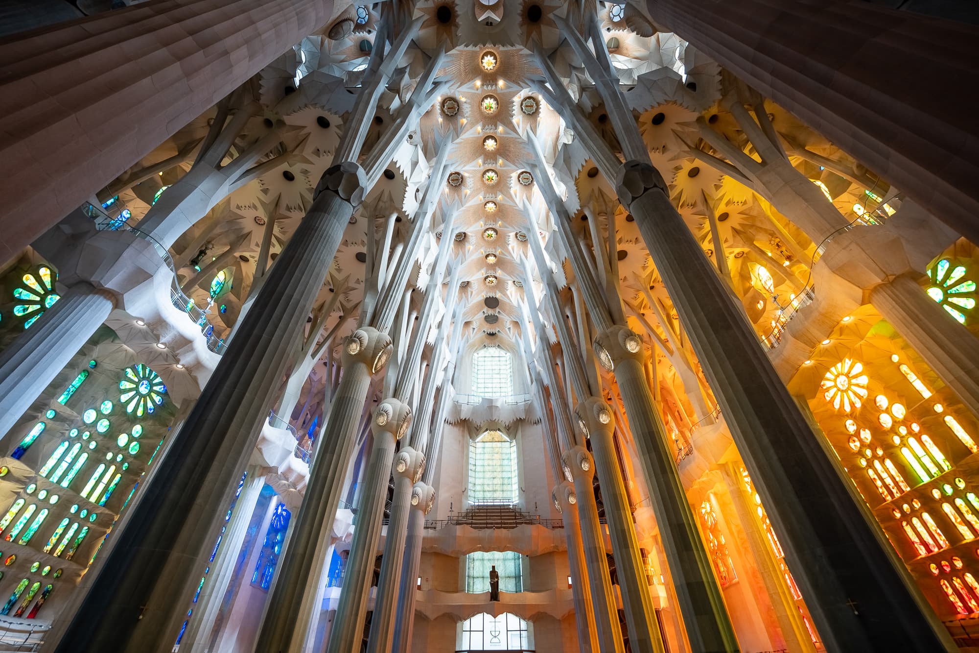 Interior of Sagrada Familia in Barcelona, with cool green and blue stained glass light on one side of the nave and warm orange and red light on the other.